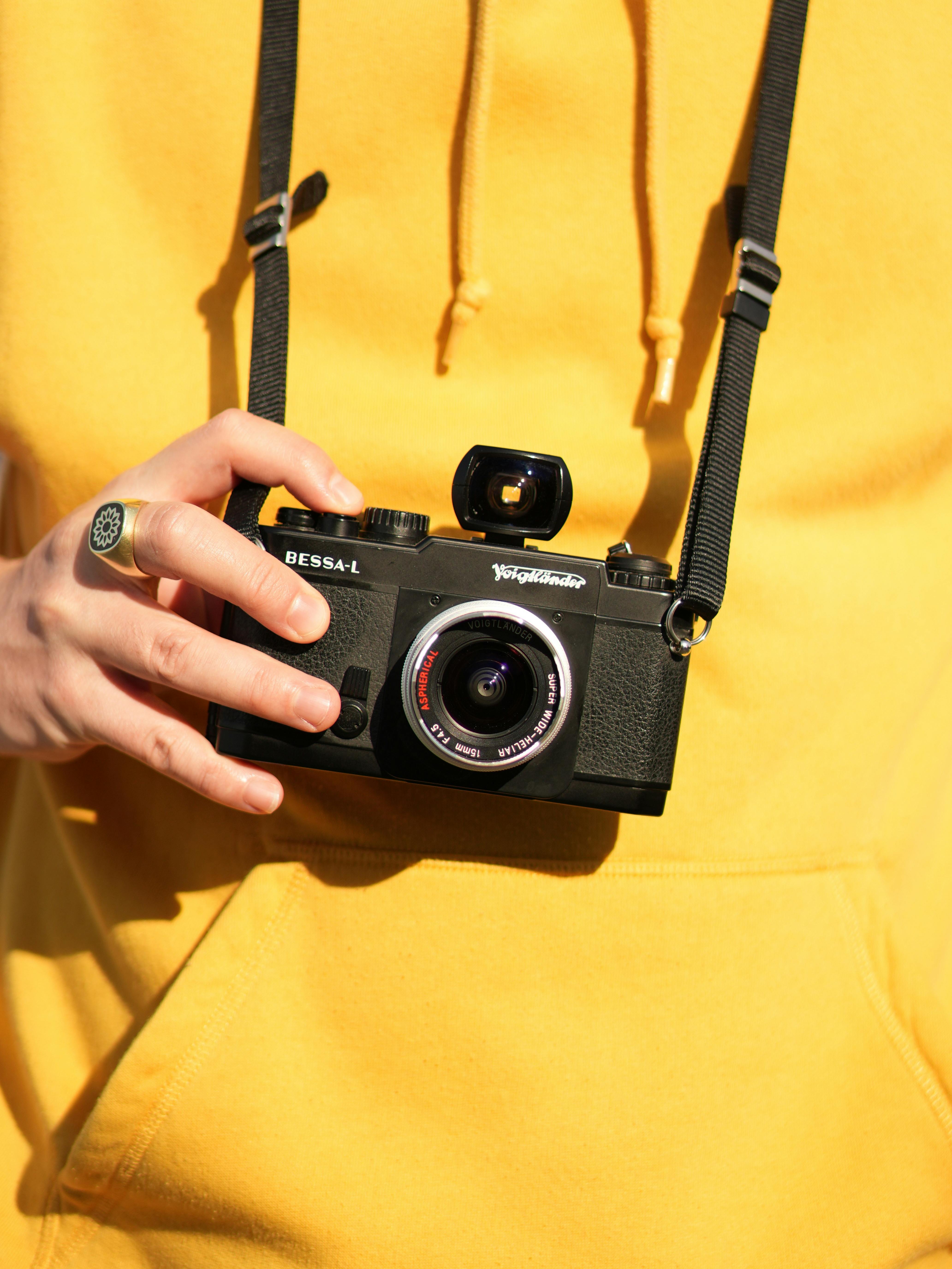 Young adult holding a Bessa-L film camera, wearing a vibrant yellow hoodie.