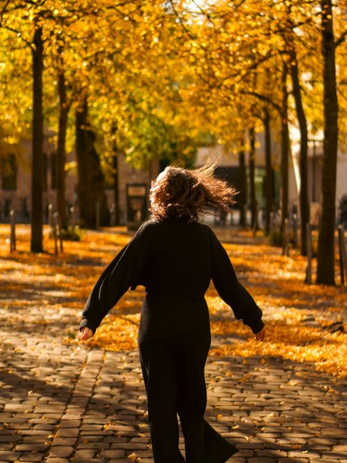 Woman gracefully walks through an autumn park with sunlight filtering through golden leaves.