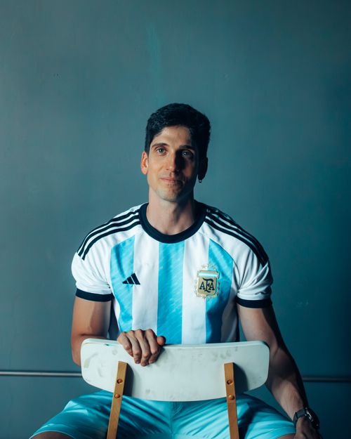 Free Adult man sitting on chair wearing Argentina soccer jersey, indoor setting. Stock Photo