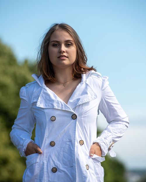Free Woman in a white coat enjoying a sunny day in a Helsinki park, capturing serene summer vibes. Stock Photo