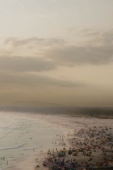 Aerial shot of a crowded beach at sunset with people enjoying the water and sand.