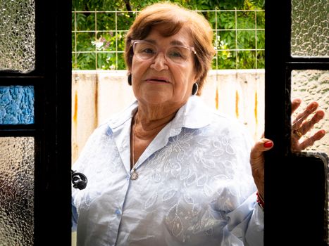 Senior woman with glasses standing in doorway, showcasing a calm expression.