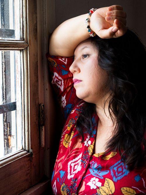 Free A woman in colorful floral attire gazes thoughtfully out of a window, capturing a moment of reflection. Stock Photo