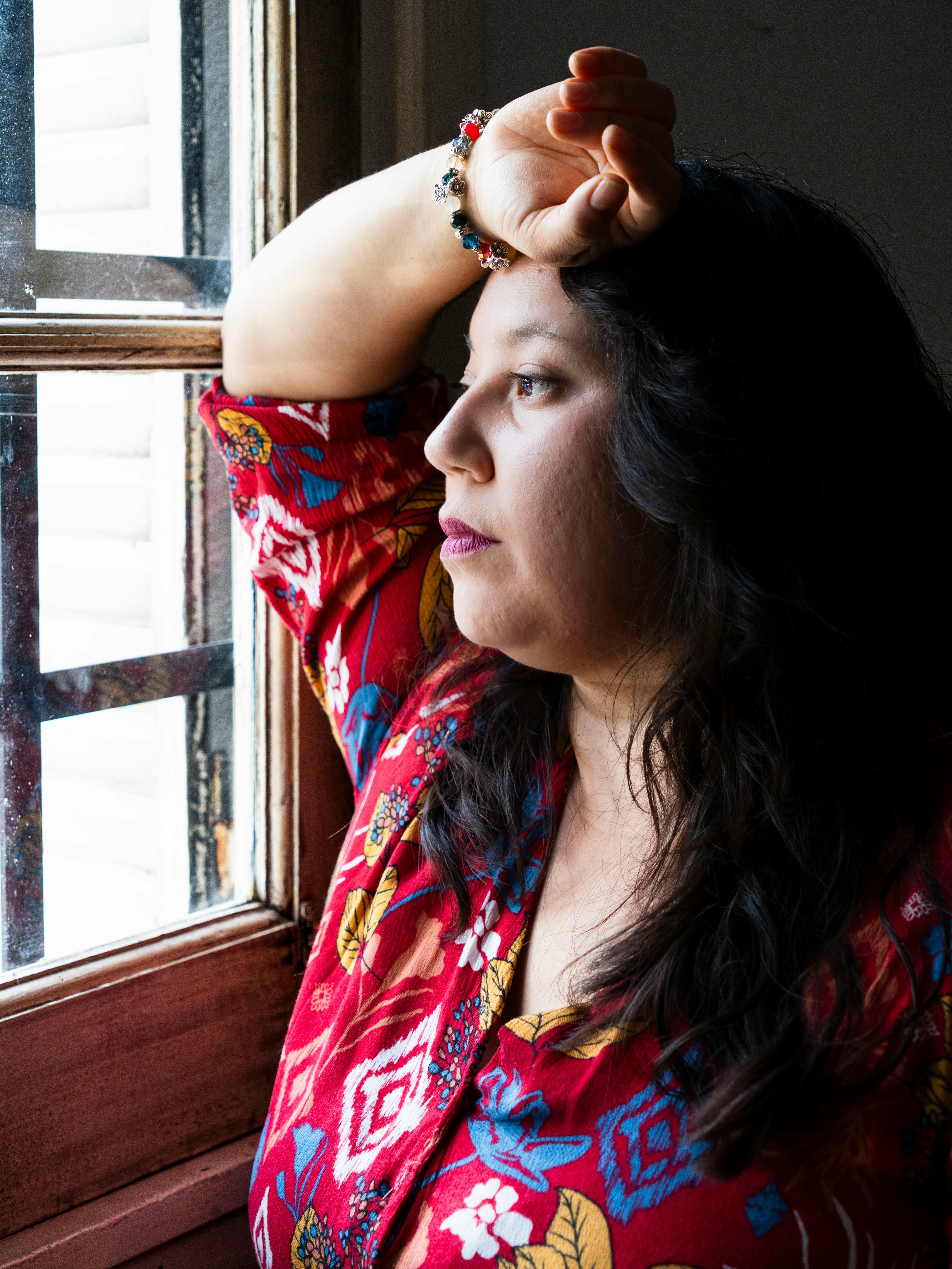 Adult woman in colorful outfit gazing out the window, lost in thought.