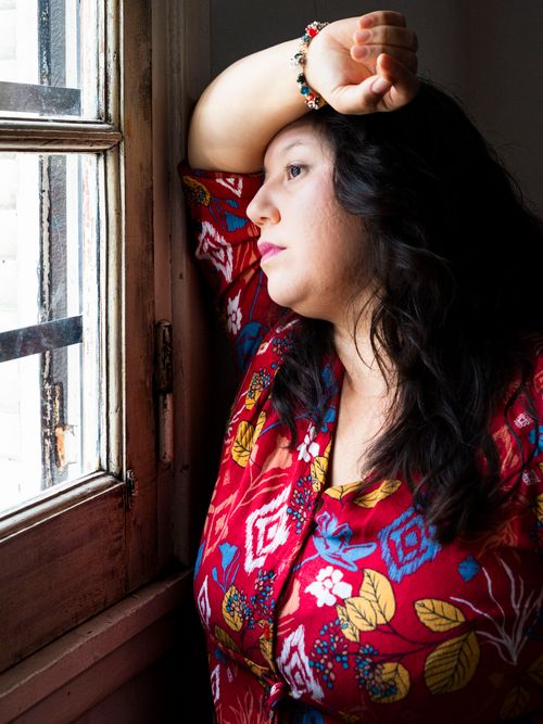 Free A thoughtful woman gazes outside through a window, wearing a vibrant floral dress. Stock Photo