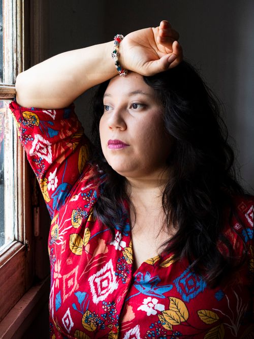 Free Thoughtful woman in vibrant floral top gazes out the window. Natural light portrait photography. Stock Photo