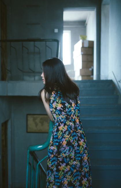 Elegant woman in a floral dress standing on an urban staircase indoors, atmospheric lighting.