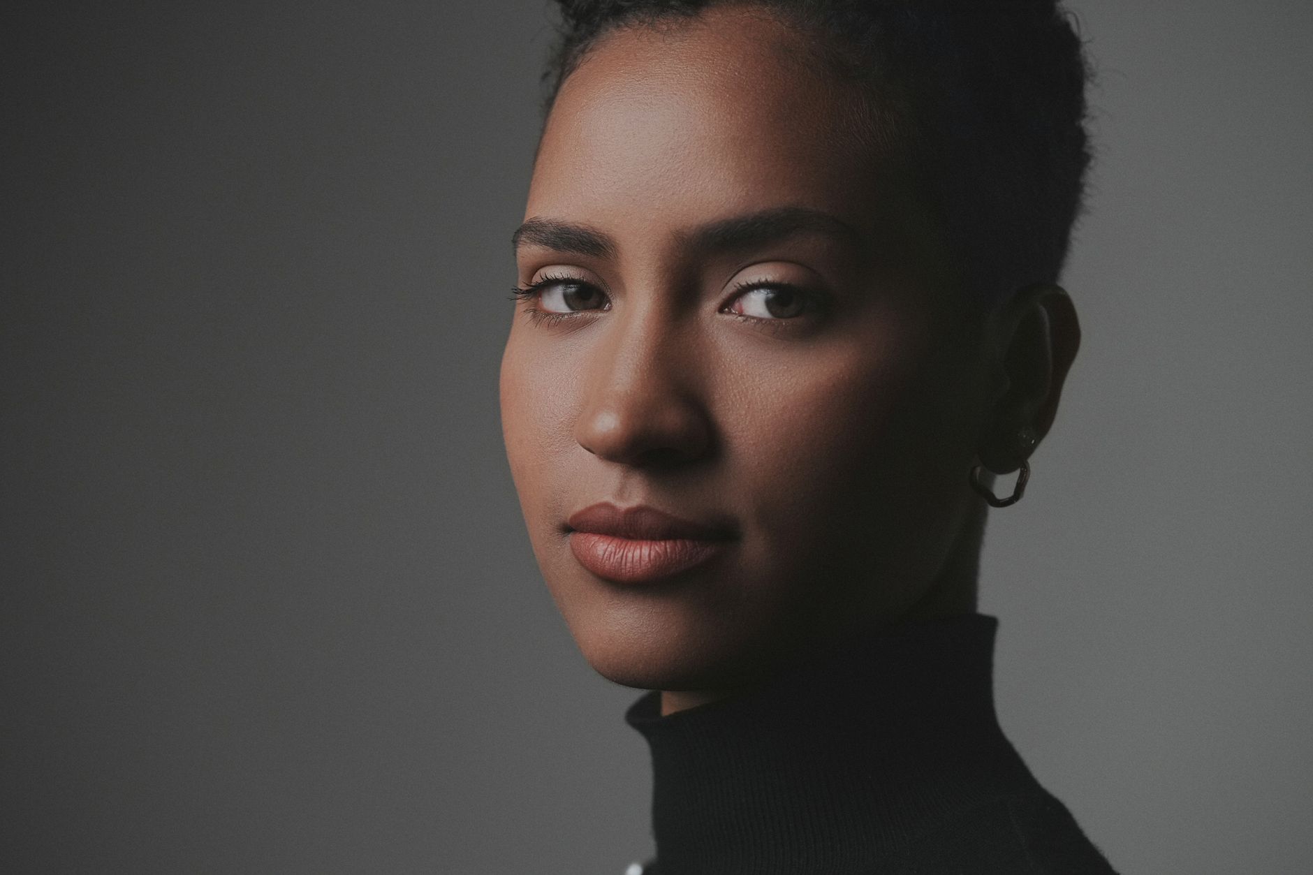 A woman wearing a black turtleneck with a confident expression in a studio setting.