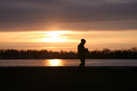 Silhouette of a person walking by a lake during a vibrant sunset, creating a serene and peaceful scene.