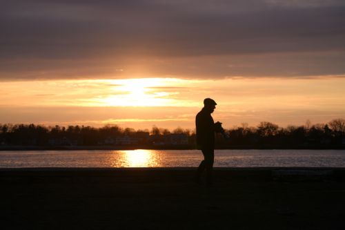 Free Silhouette of a person walking by a lake during a vibrant sunset, creating a serene and peaceful scene. Stock Photo