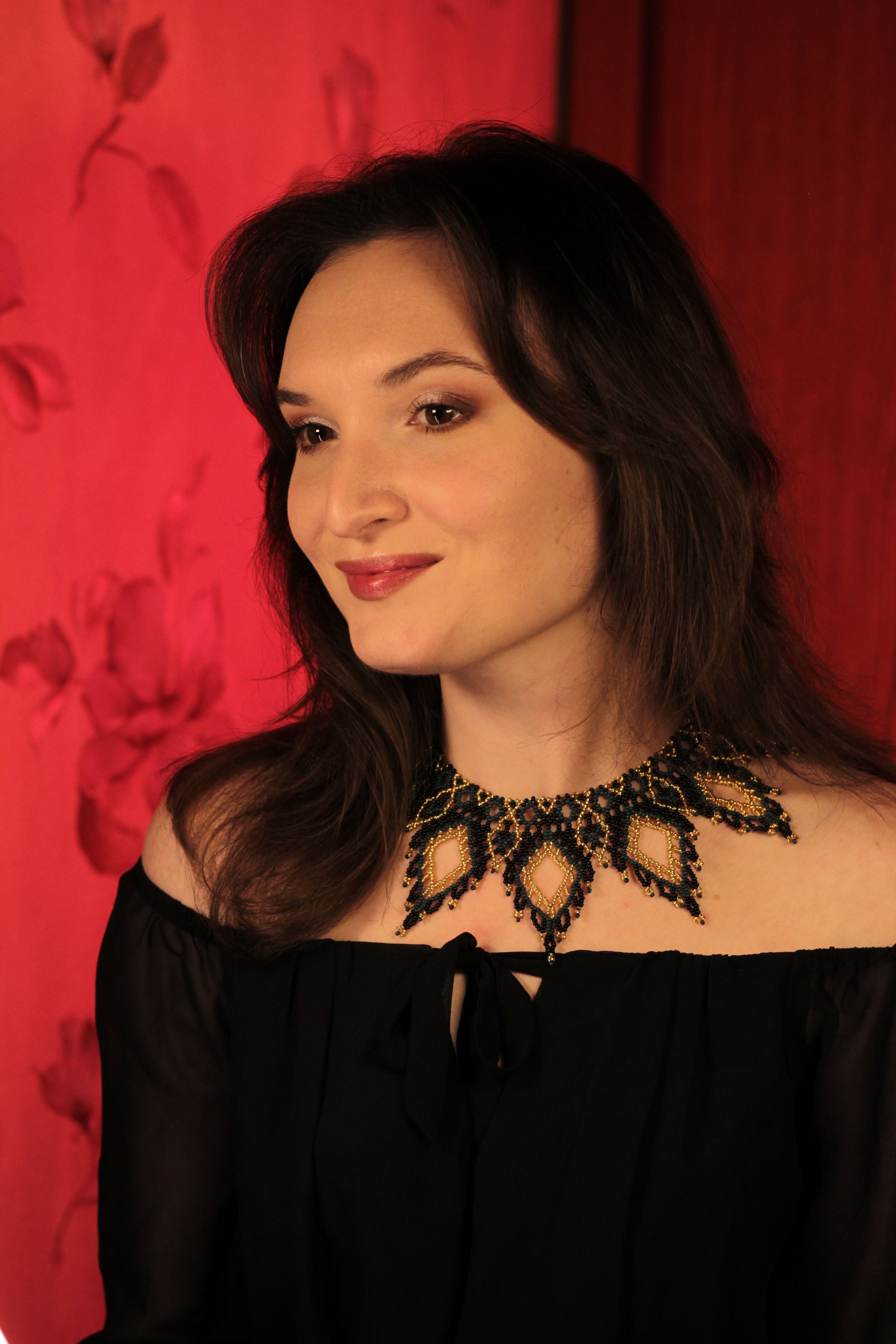Woman in black dress with statement necklace against a red background.