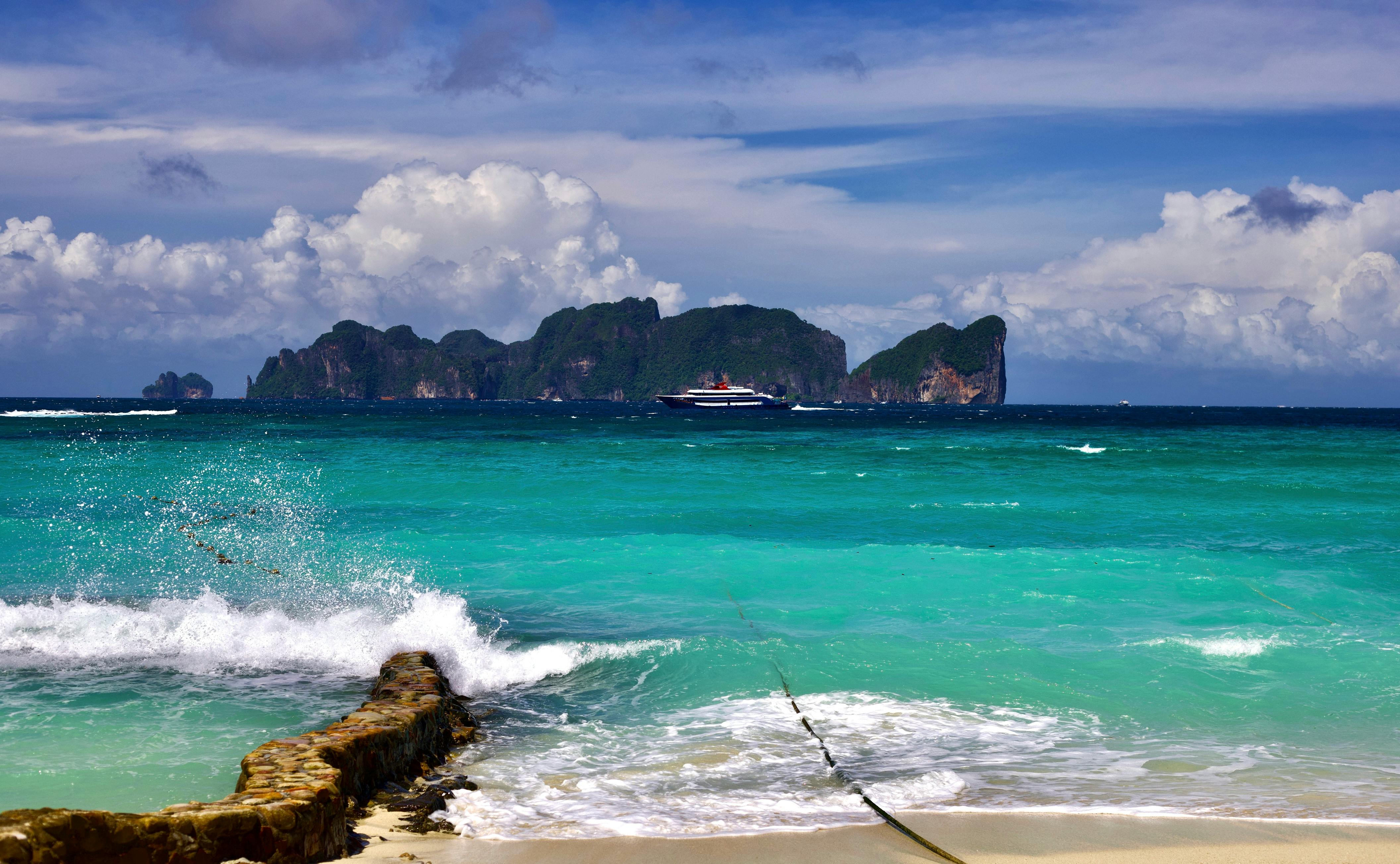 Scène de plage époustouflante avec des eaux turquoises, une île lointaine et un ciel dégagé. Parfait pour des escapades tropicales.