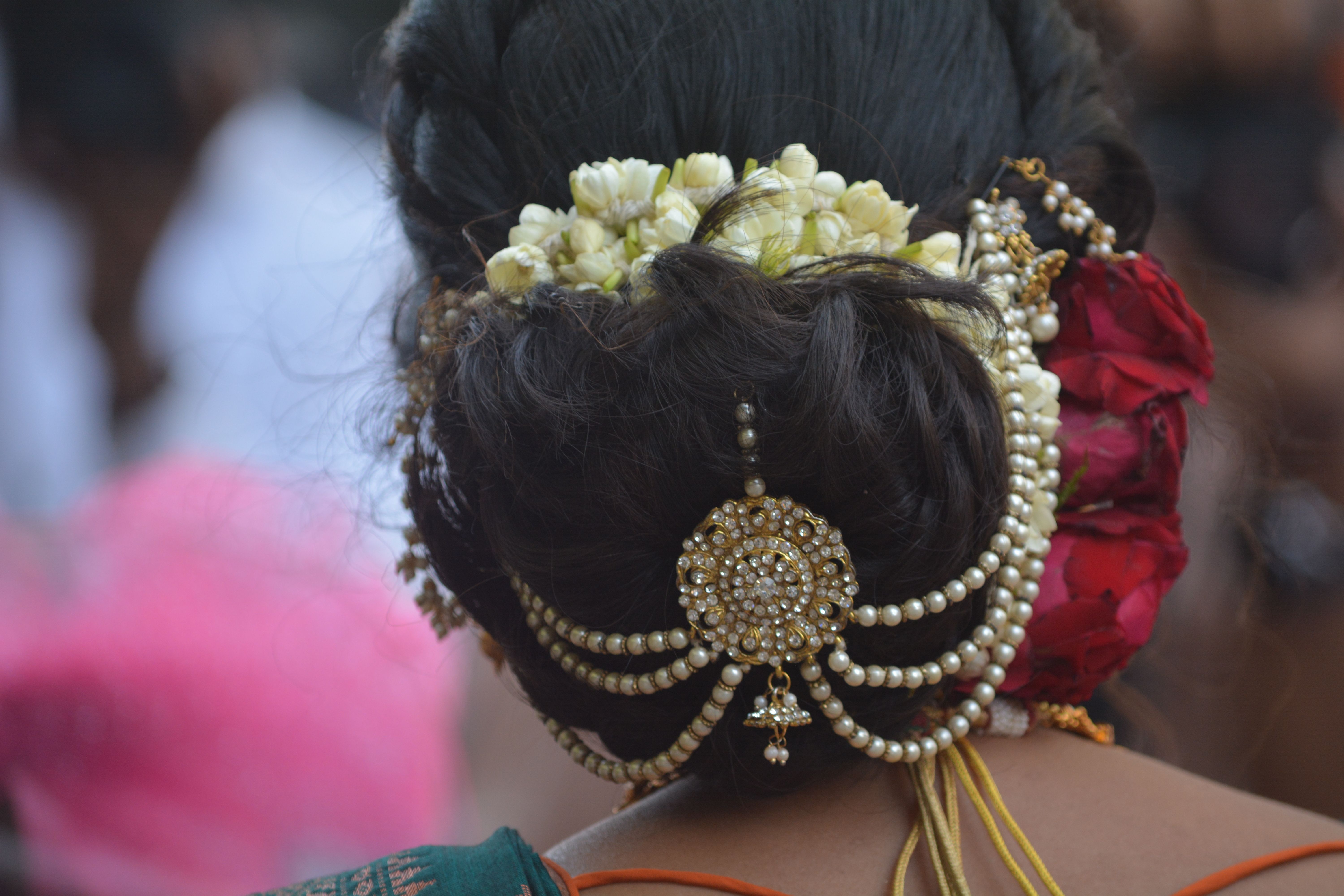 Close-up of a bride's hair bun adorned with jasmine flowers, pearls, and gold ornaments - traditional Nalangu jewellery