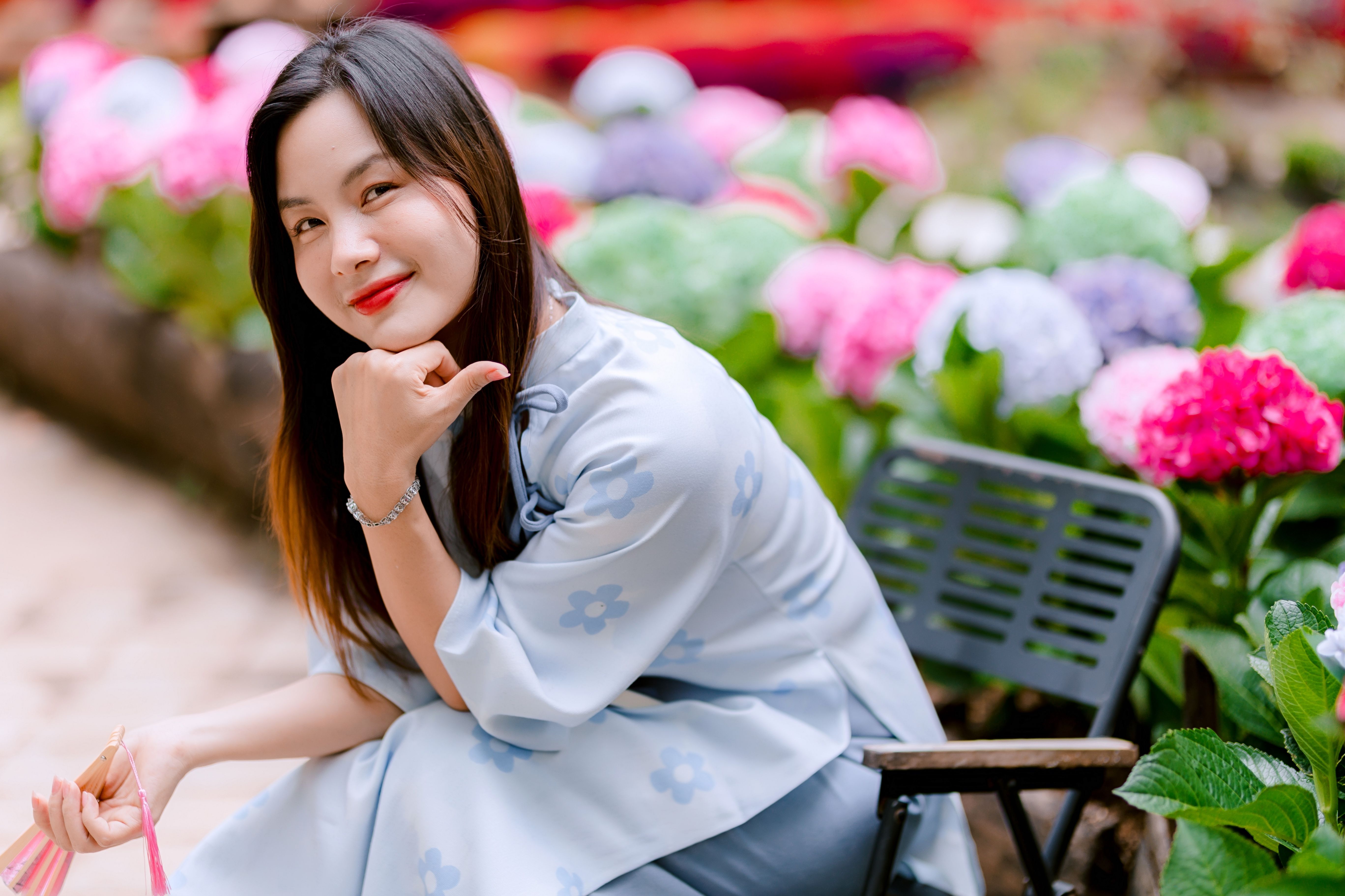Asian woman posing in garden with vibrant hydrangea blossoms, exuding cheerful elegance.