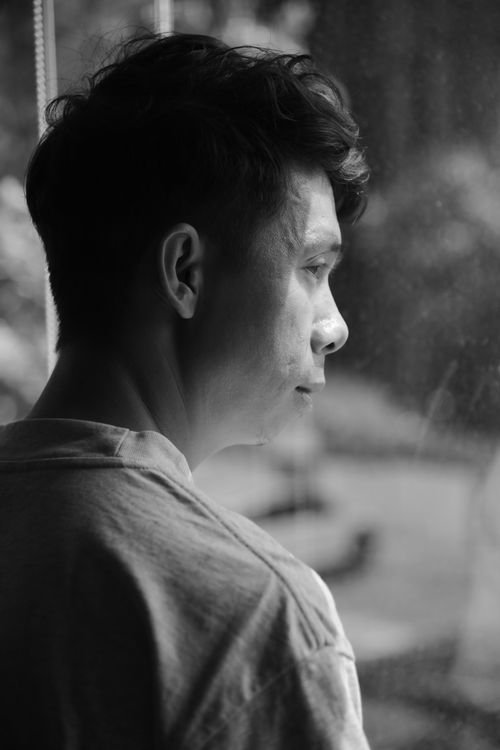 Free Black and white portrait of a contemplative young adult man looking out a window. Stock Photo