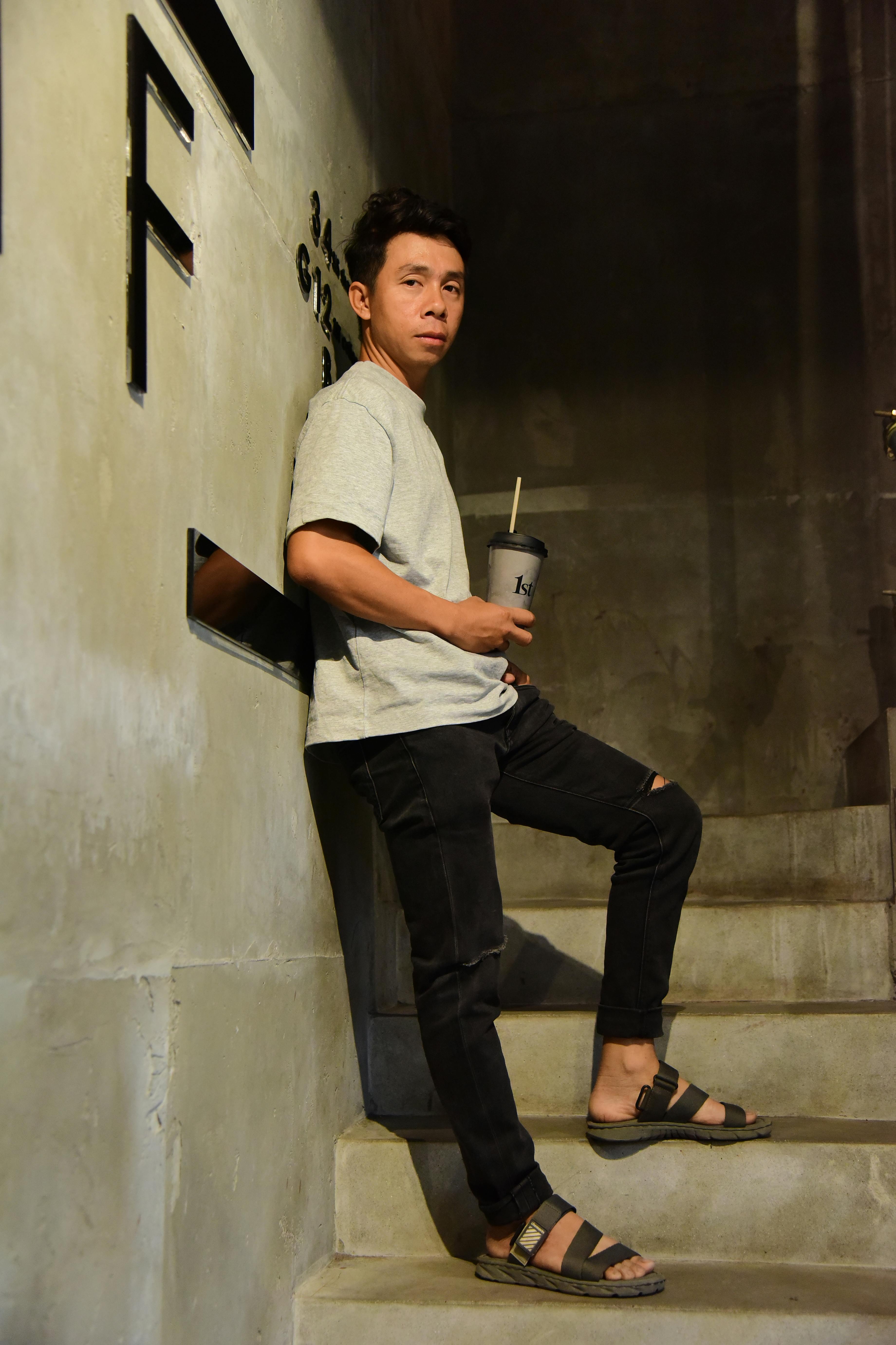 A man in casual attire leans against a wall on a staircase holding a drink.