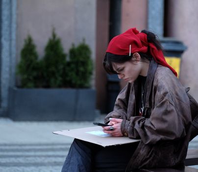 Woman in casual clothing using a smartphone while sitting outdoors. Street scene with a focused expression.