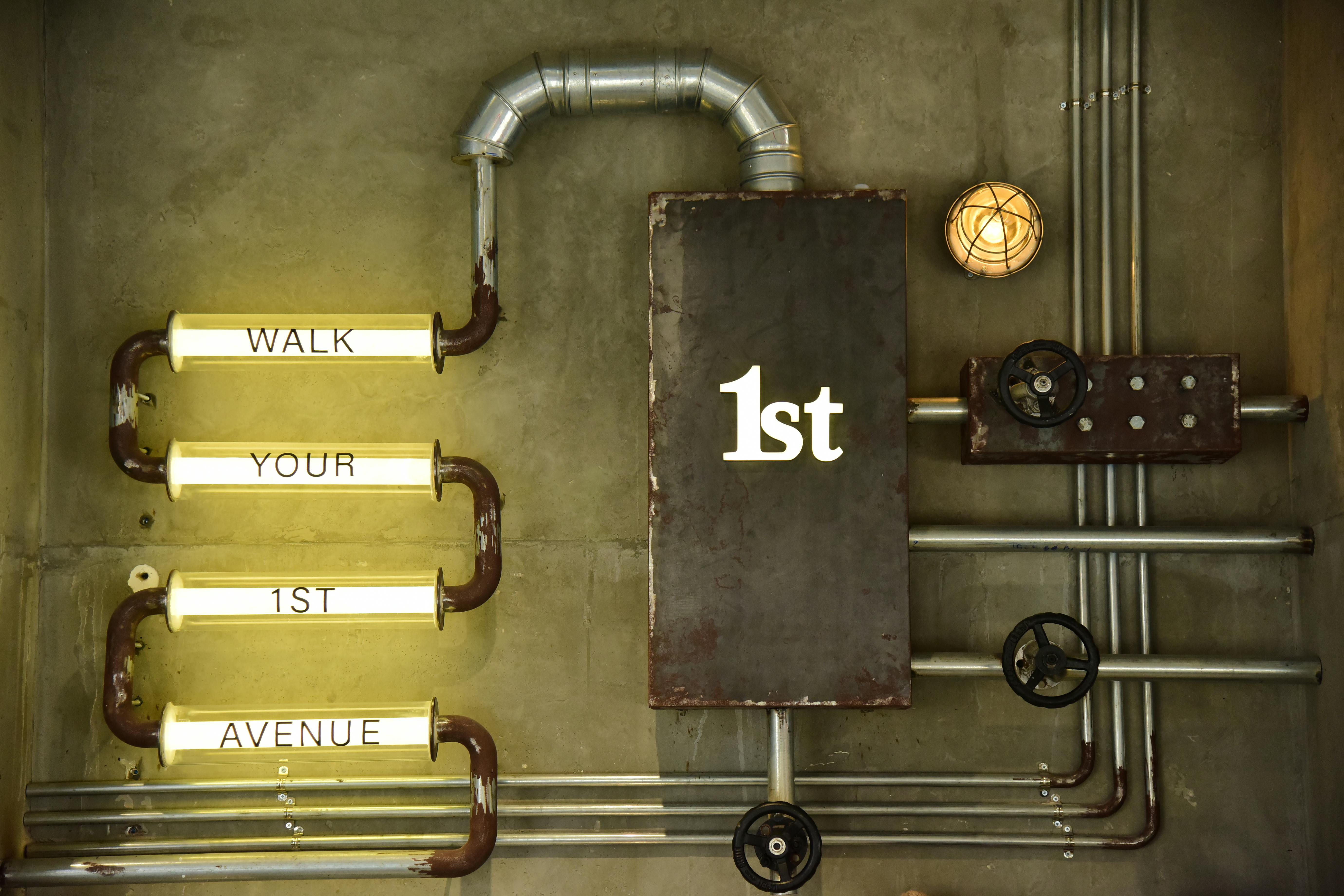 An artistic industrial wall design featuring metal pipes and illuminated words.