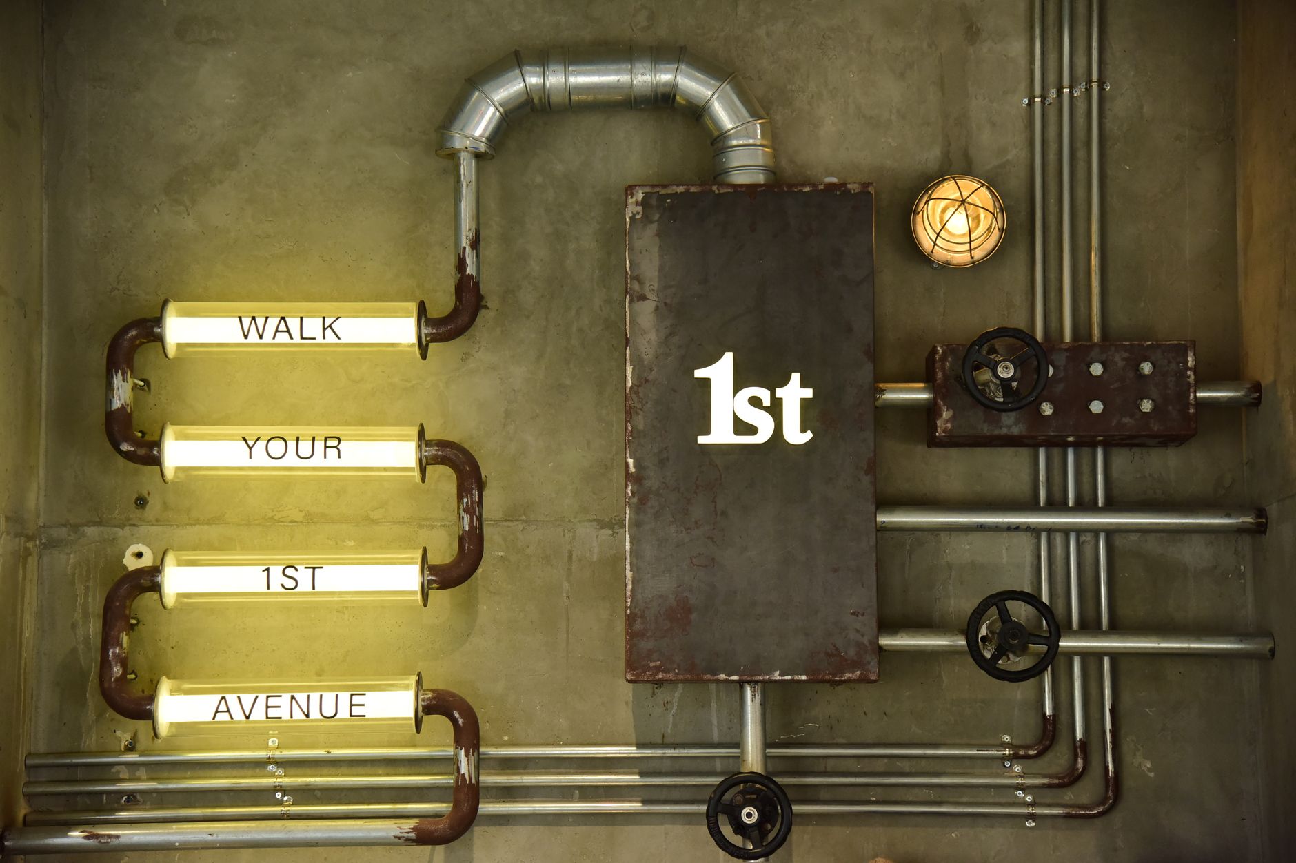 An artistic industrial wall design featuring metal pipes and illuminated words.