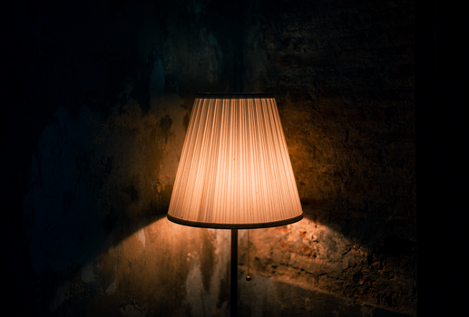 Warmly lit lamp casting shadows on a textured wall in a dark, moody setting.