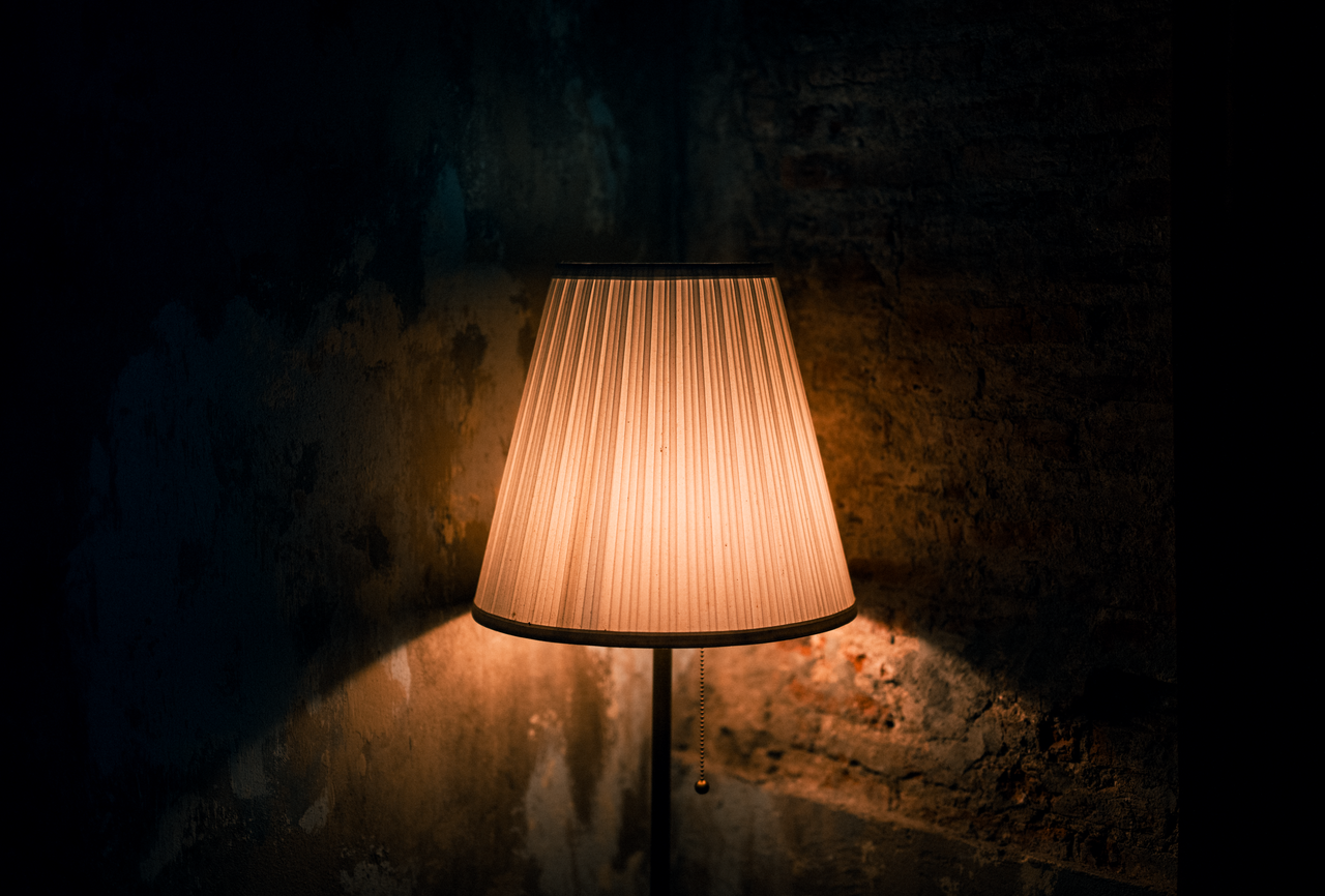 warmly lit lamp casting shadows on a textured wall in a dark moody set