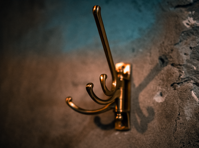 A close-up of a brass wall hook casting a shadow on a textured wall