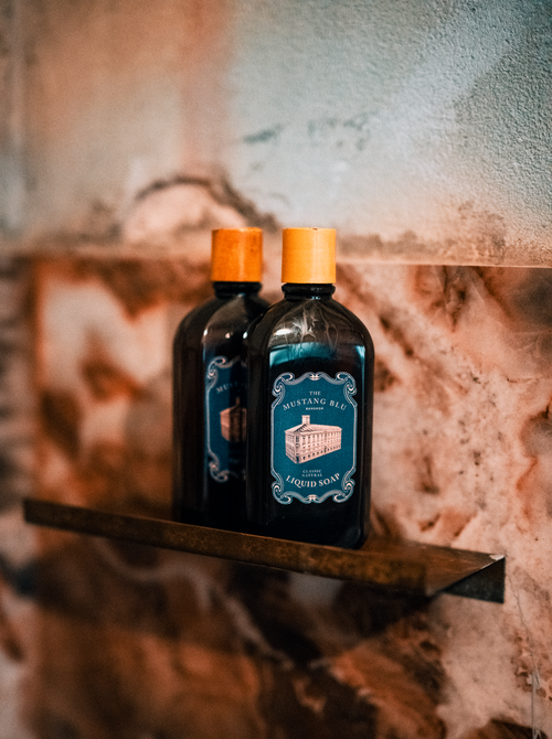 Free Elegant liquid soap bottles displayed on a marble shelf in a modern bathroom setting. Stock Photo