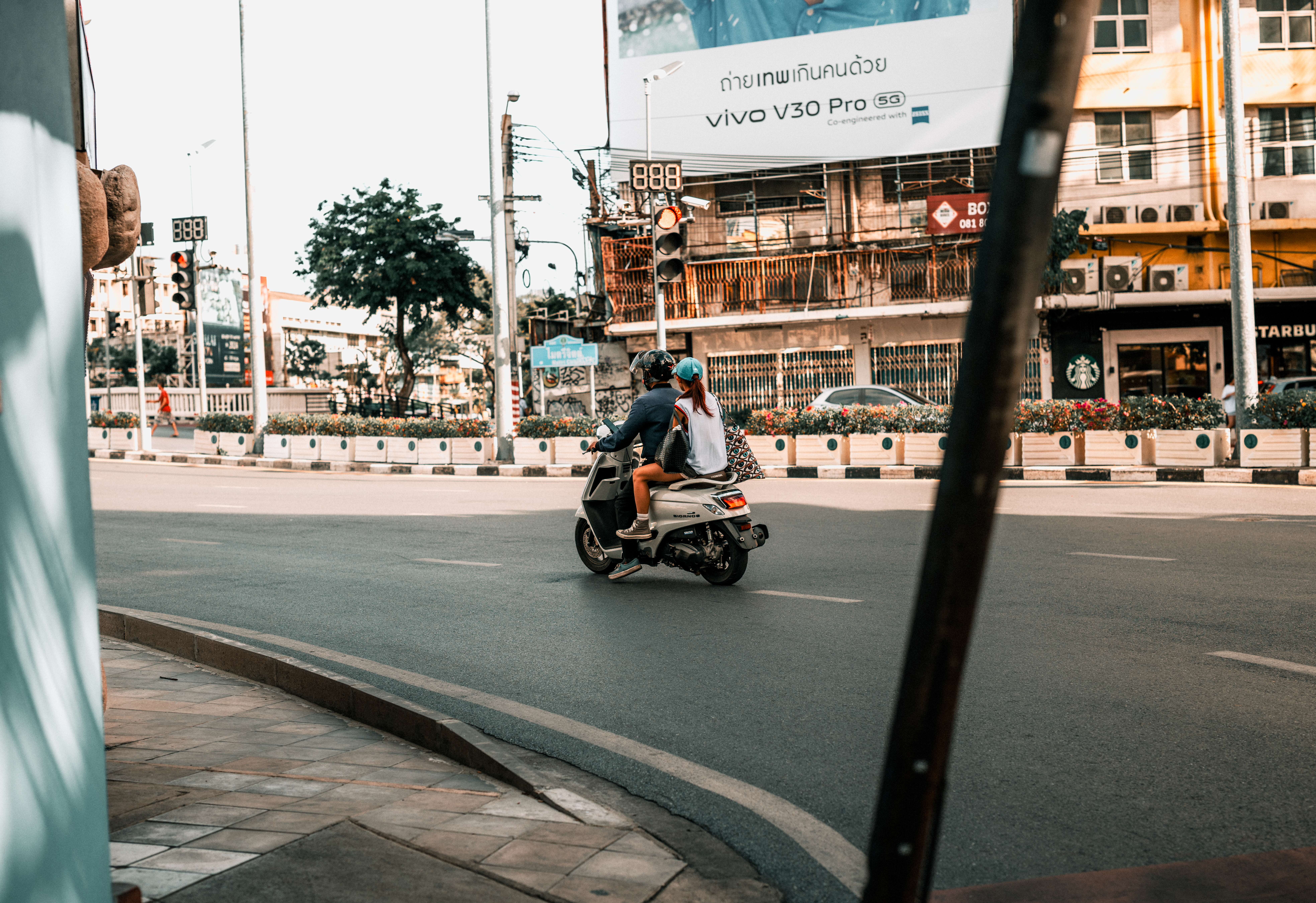 Couple on a motorbike navigating a busy Bangkok street with urban backdrop.