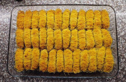 Glass tray filled with golden kataifi pastry rolls on a granite countertop, ready for baking.