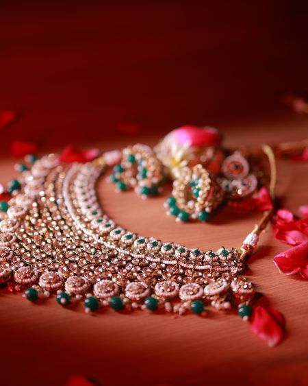 Rose-gold necklace and earrings with emerald drops resting on red rose petals