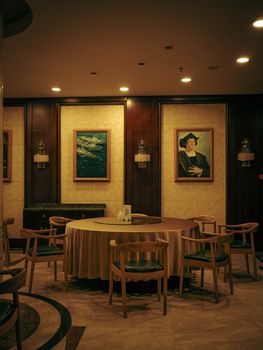 Stylish dining room setup with round table, wooden chairs, and classic paintings on the wall.