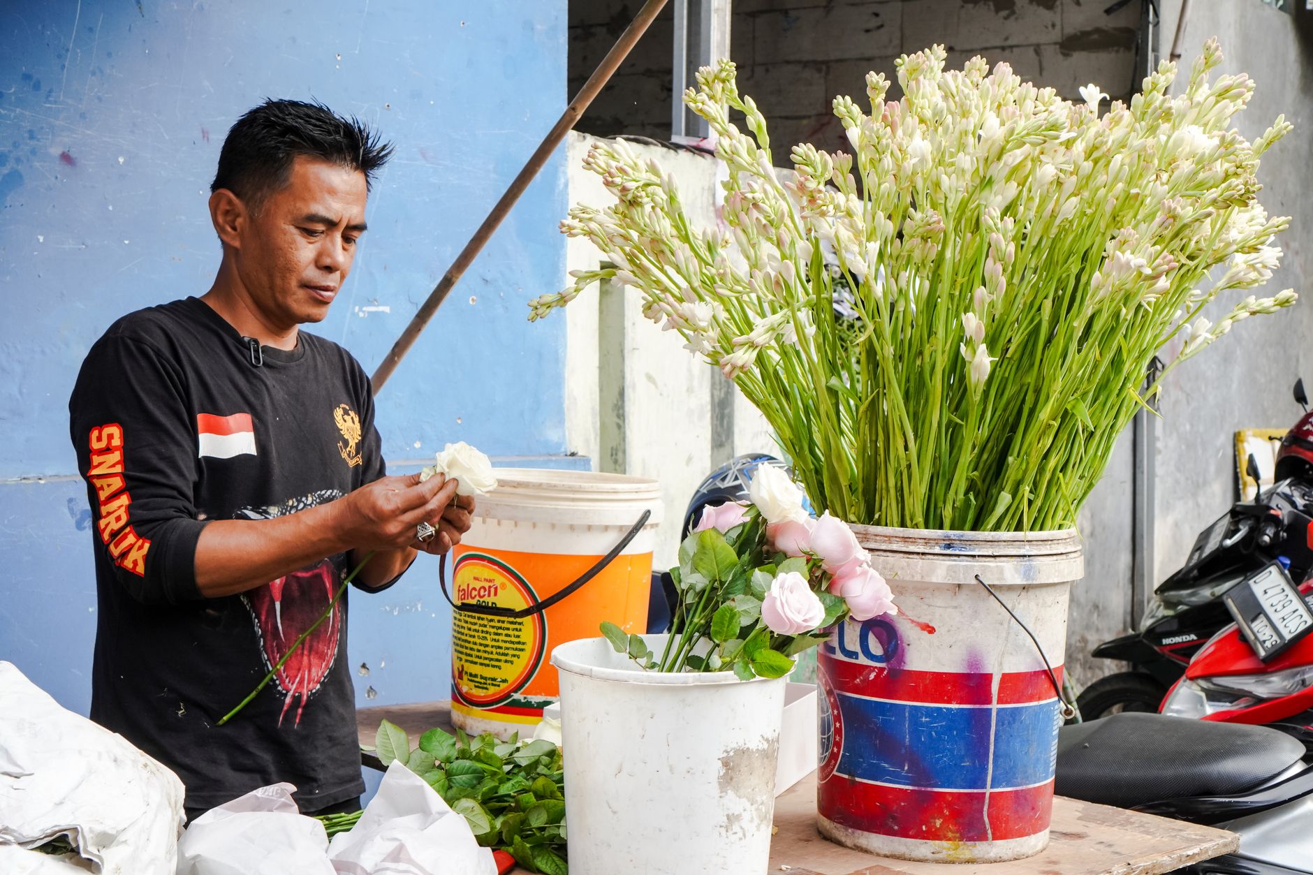 Indonesian florist arranging fresh flowers at an outdoor market stall.