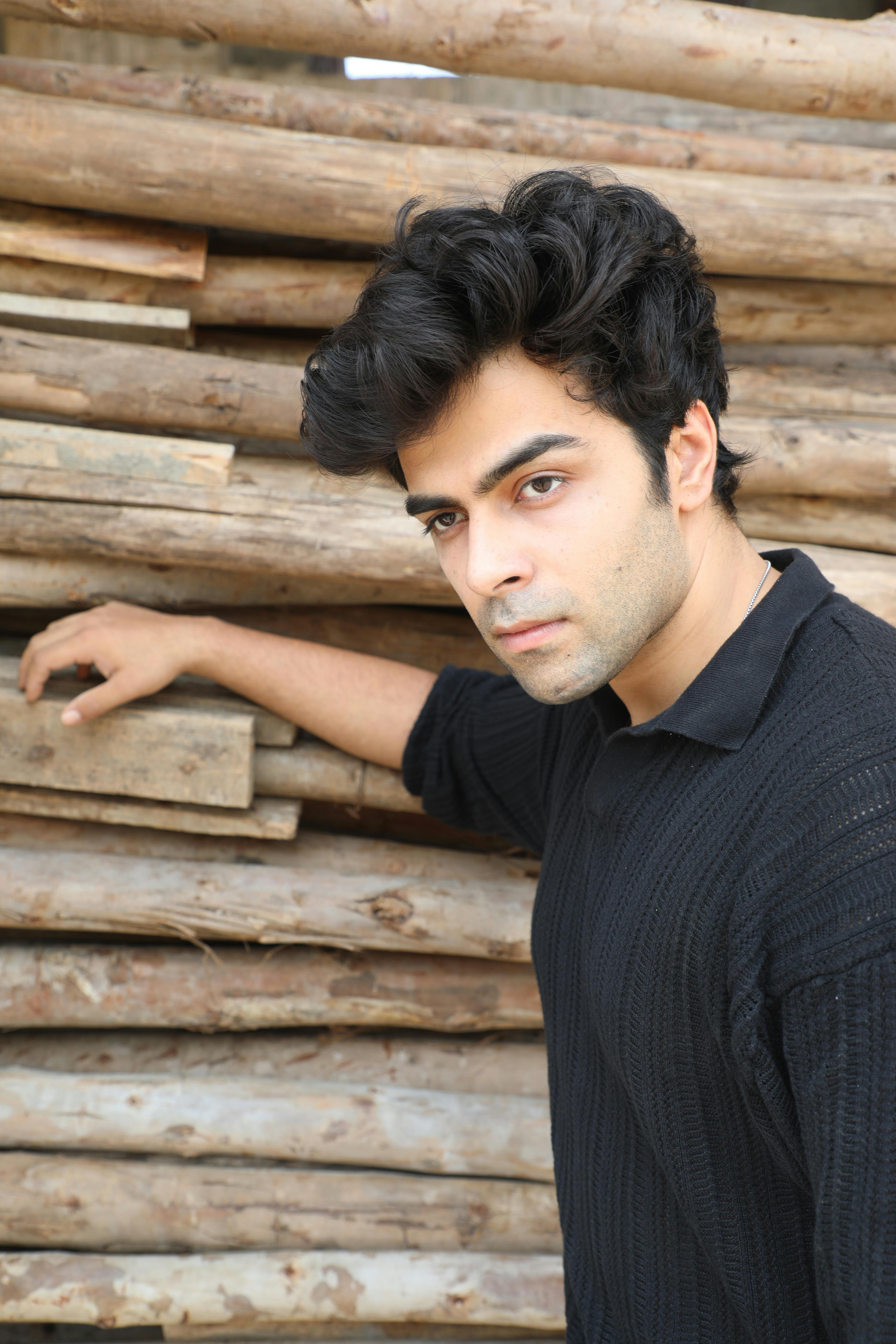 Young man posing beside a stack of logs, showcasing a confident expression.