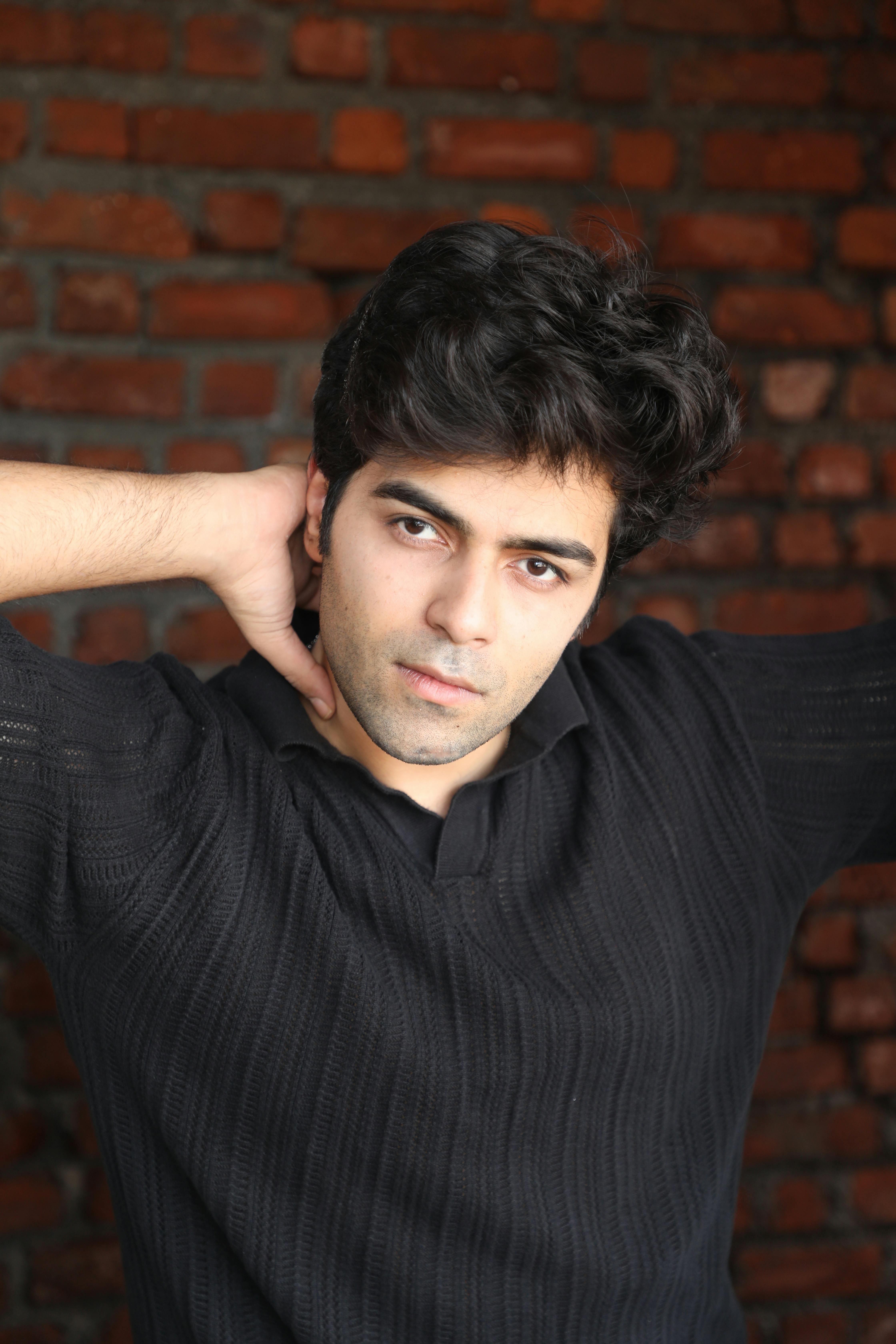 Close-up portrait of a man in a black sweater posing in front of a brick wall.