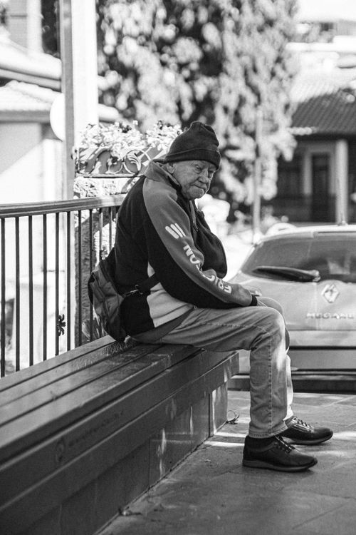 Free Black and white photo of an elderly man sitting on a bench outdoors. Thoughtful expression. Stock Photo