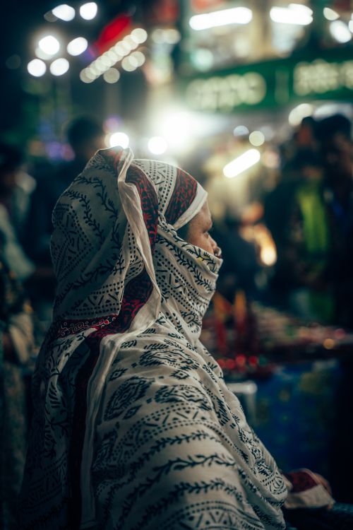 Free A woman in traditional attire browsing a vibrant night market, filled with lights and people. Stock Photo