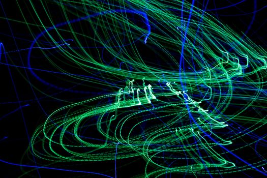 Vibrant abstract light trails in motion with green and blue hues against a dark background.