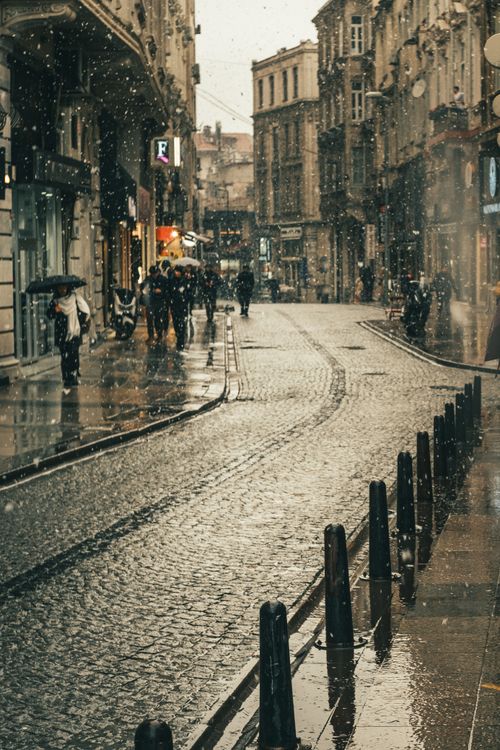 Free Historic cobblestone street in rain with people using umbrellas. Urban cityscape vibe. Stock Photo