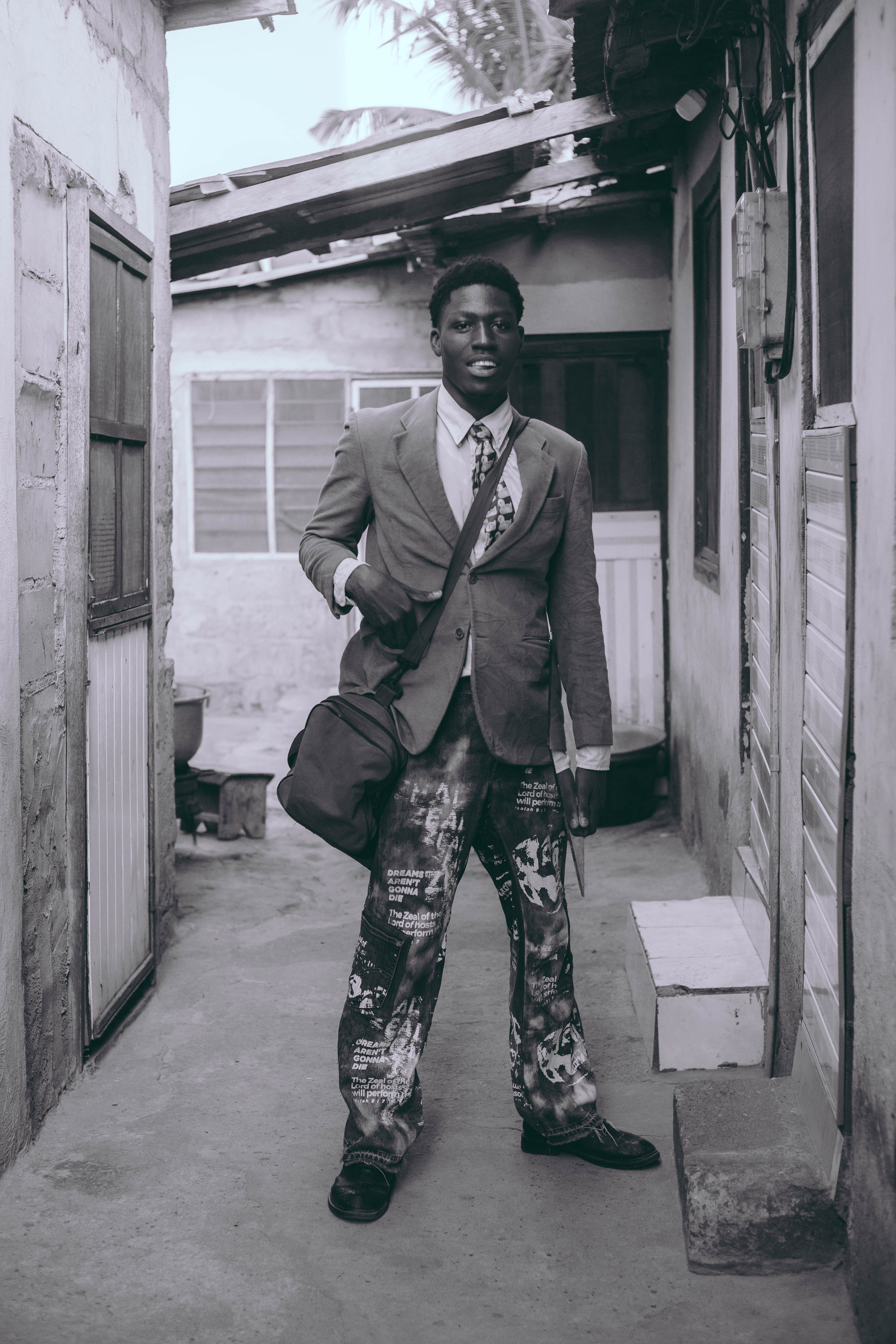 Black and white portrait of a stylish man standing confidently in an urban alleyway in Accra.