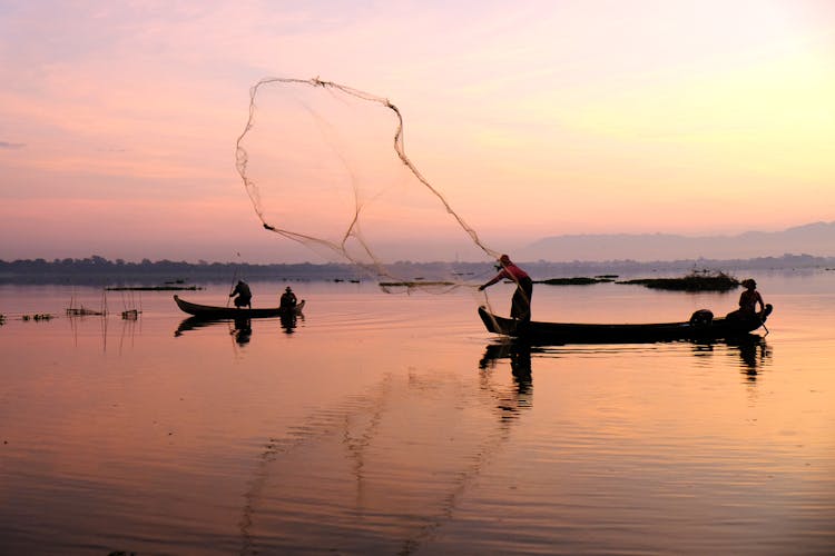 Fisherman Throwing Net Into Body Of Water