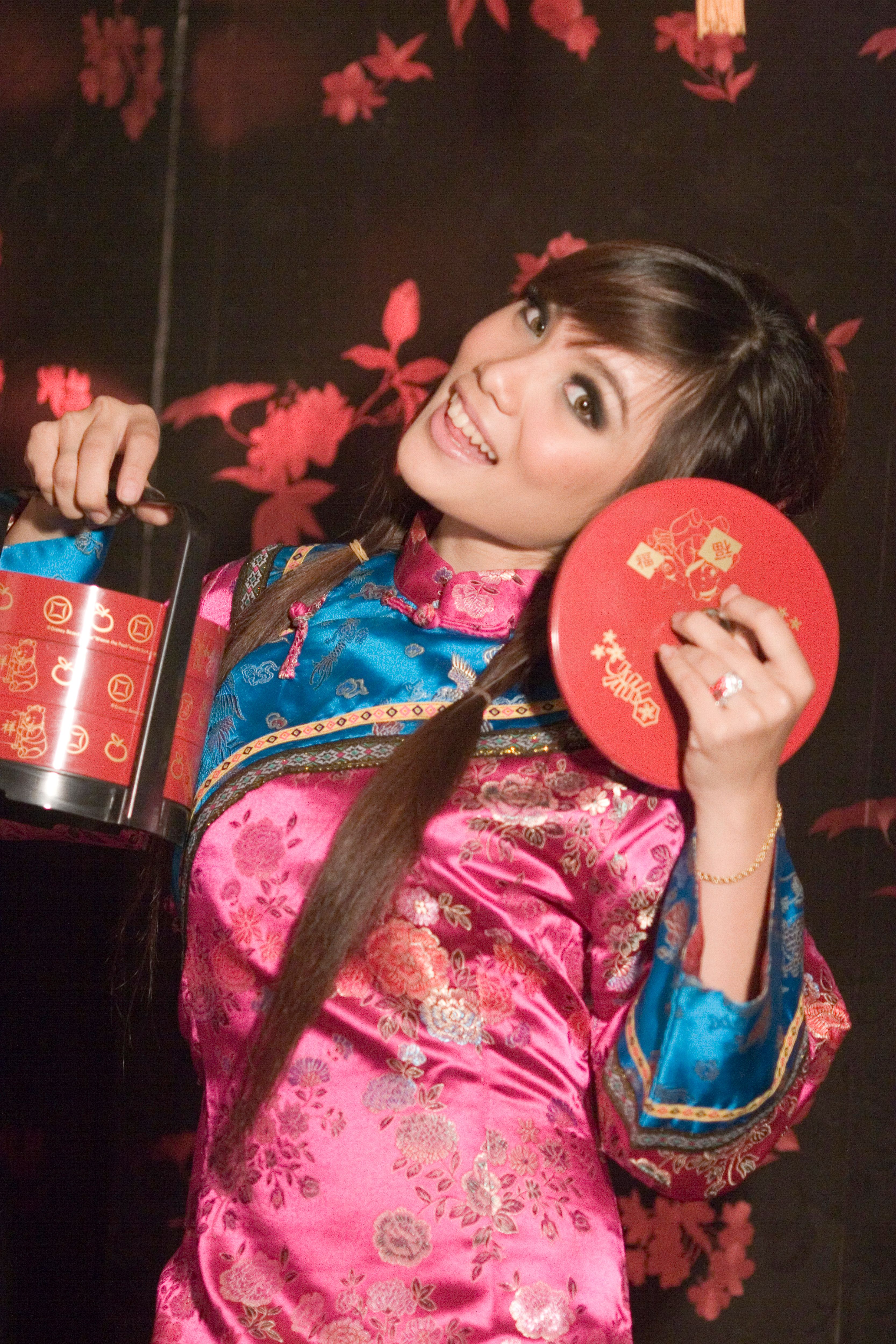 Woman in vibrant pink traditional dress holding festive red container, celebrating Chinese festival.