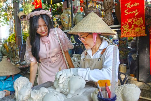 Artisan and woman in traditional Vietnamese attire crafting pottery, displaying cultural heritage.