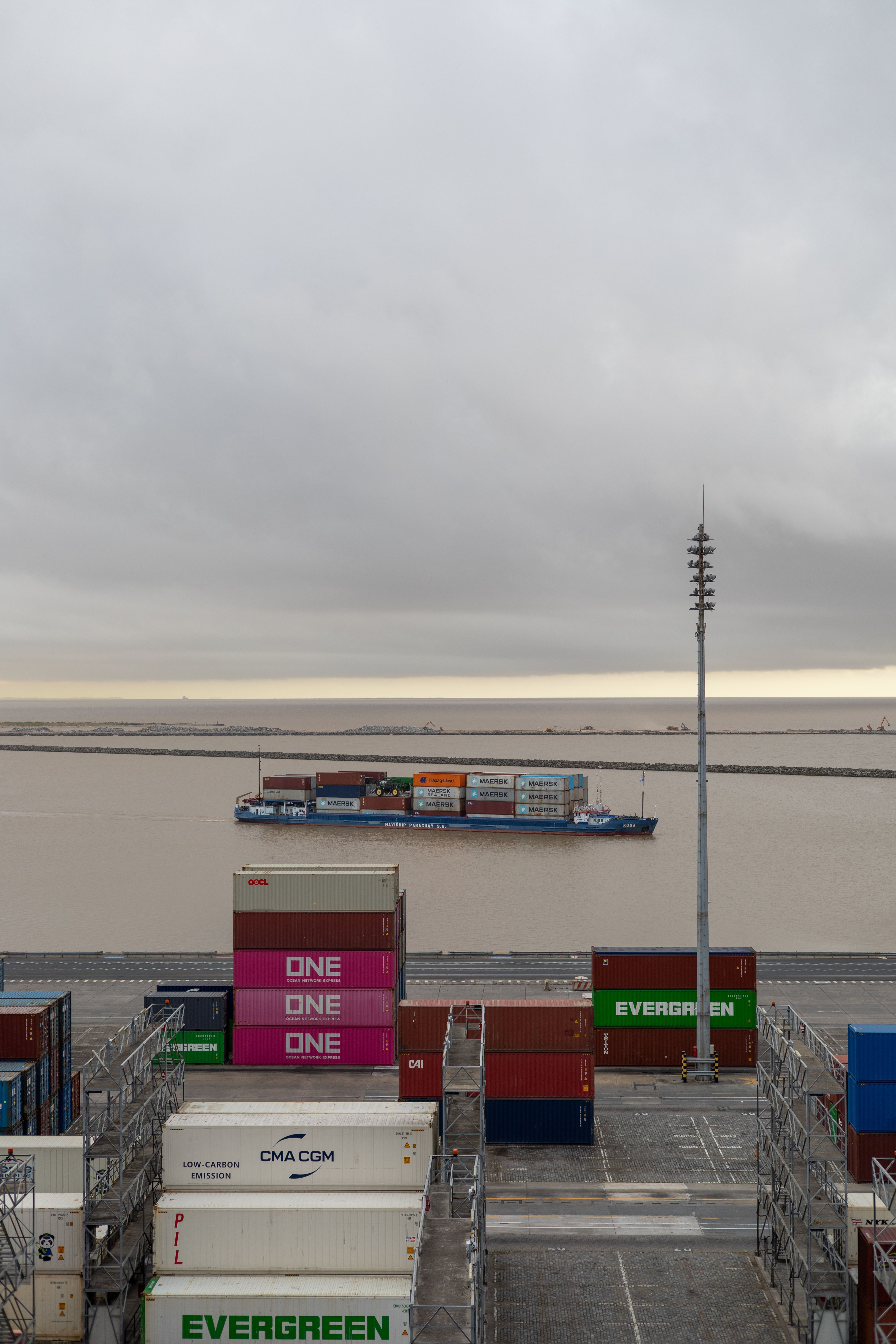 Een vrachtschip vaart door een drukke haven, omringd door kleurrijke zeecontainers.