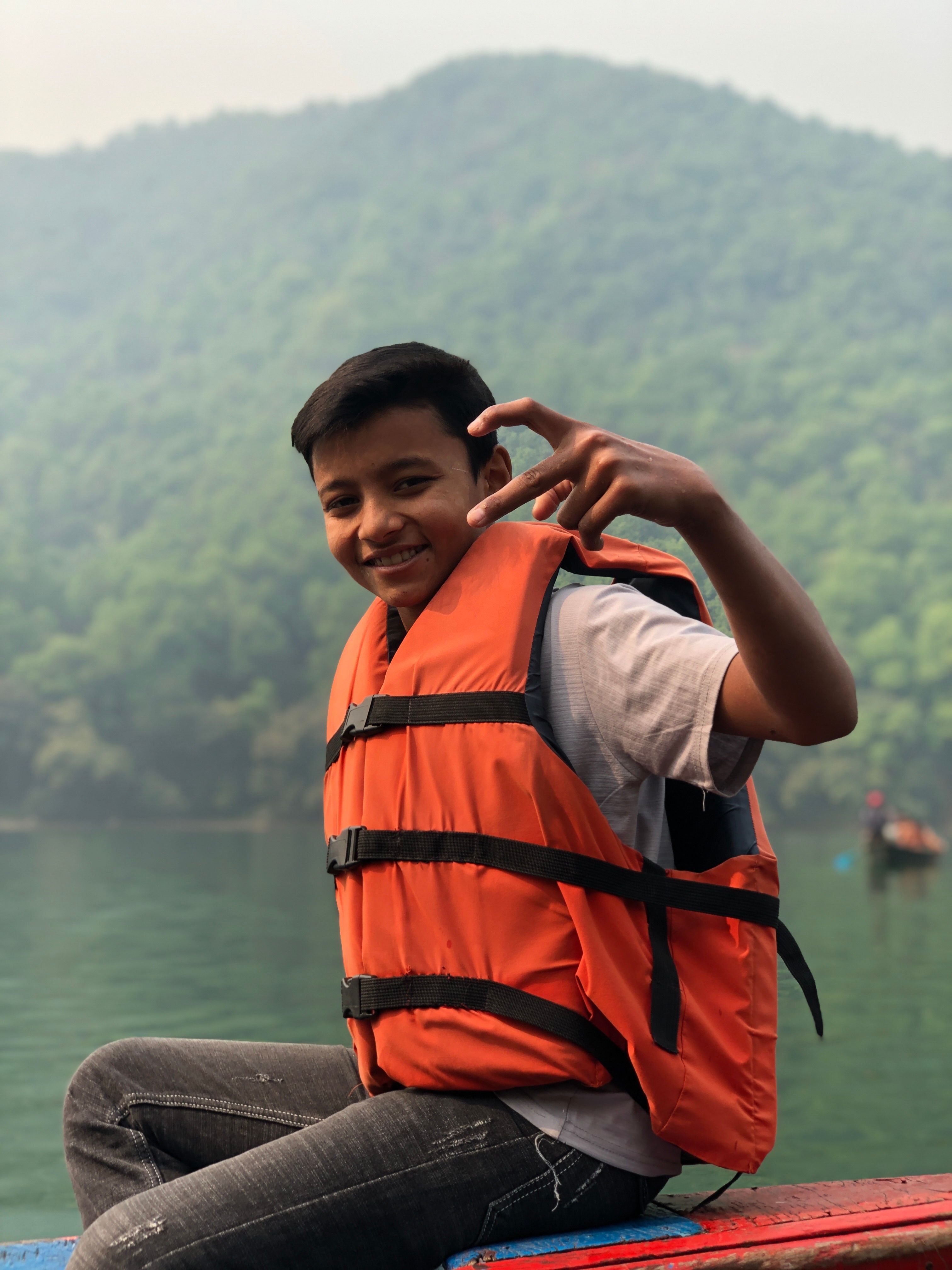 Happy teenager wearing a life vest poses on a lake with forested hills in the background.