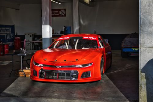 Free A vivid red stock car in a garage setting, featuring sleek design and racing elements. Stock Photo