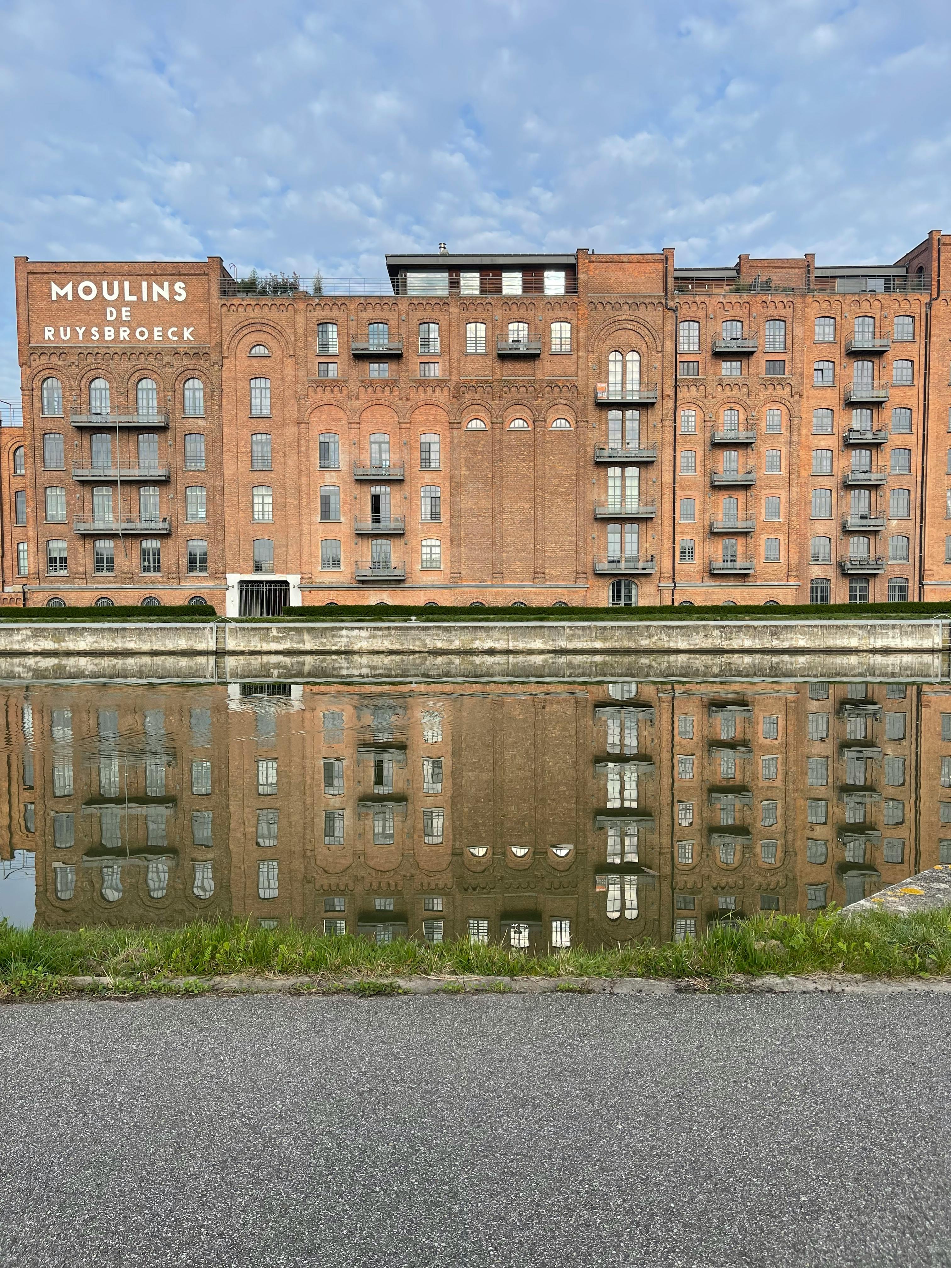 Stunning reflection of the Moulins de Ruysbroeck building in tranquil water at daytime.