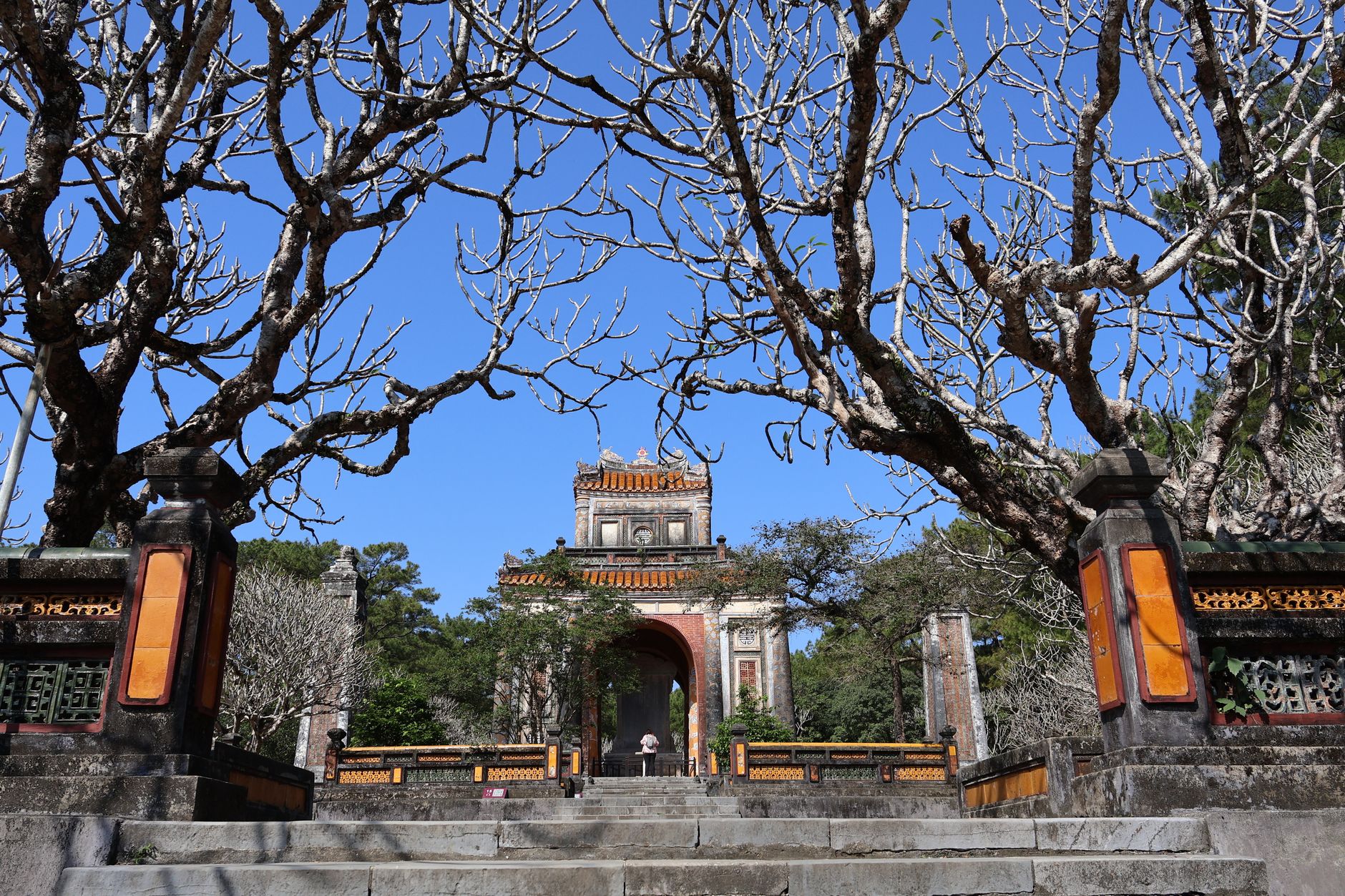 The majestic entrance of Minh Mang Tomb framed by bare trees in Hue, Vietnam.