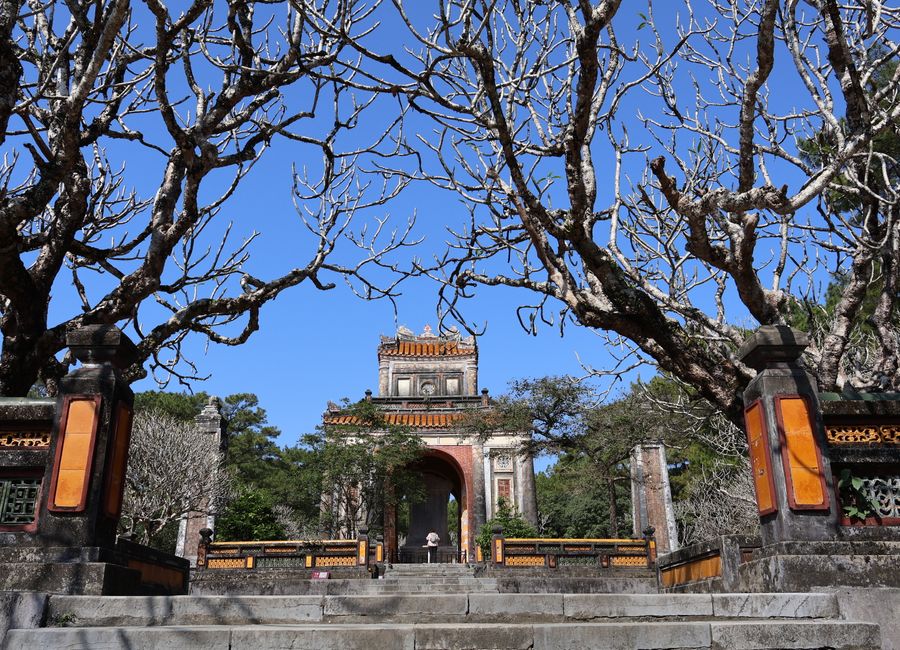 The majestic entrance of Minh Mang Tomb framed by bare trees in Hue, Vietnam.