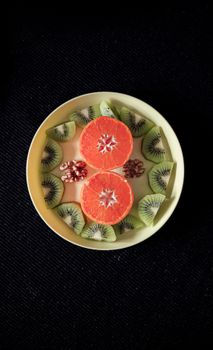Artistic arrangement of grapefruit, kiwi, and walnuts on a yellow plate, black background.