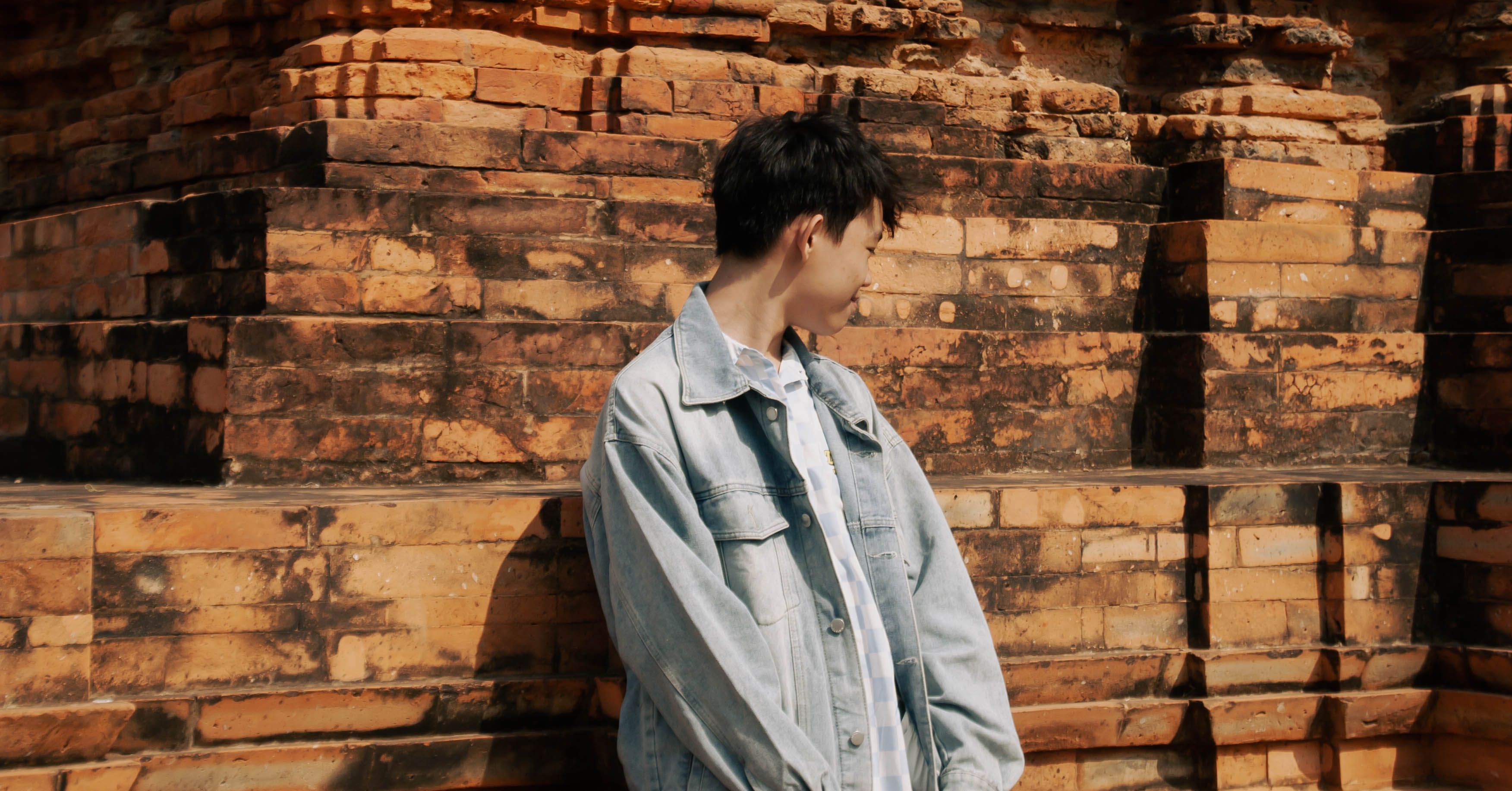 Young man in denim jacket by ancient brick wall · Free Stock Photo